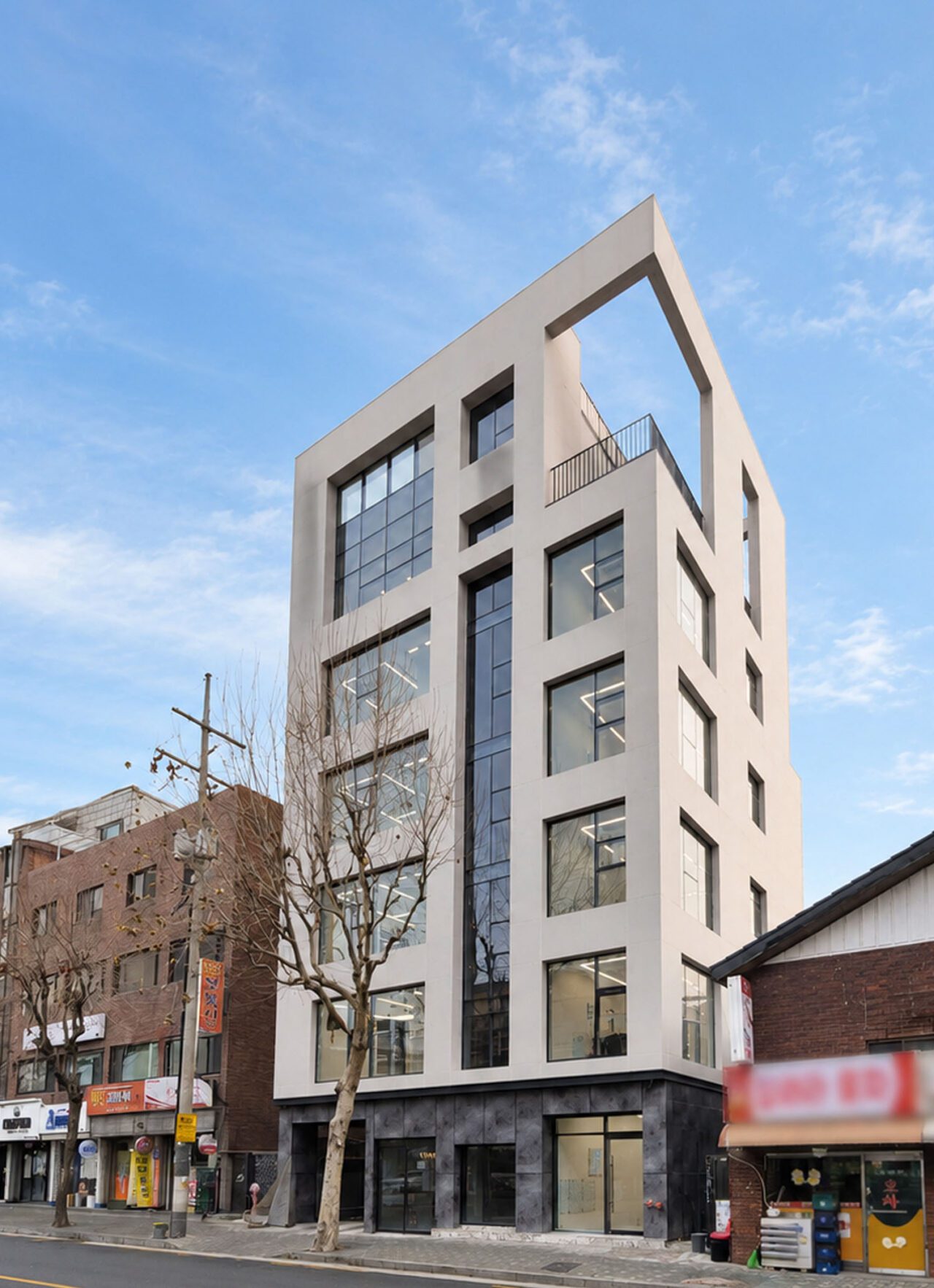 성산동 근린생활시설 증축·대수선 후 도로에서 올려다본 건물의 밝은 색상 입면과 세로로 배열된 창호, 최상층 외부공간